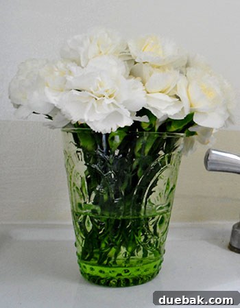 May Bloom Bonanza 7 Close-up of cream carnations in a green glass, showing stems
