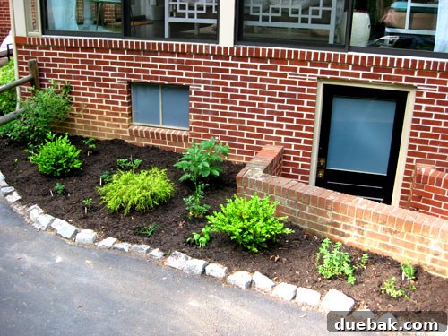 A freshly mulched edible garden with various herbs and vegetables, labeled with popsicle sticks