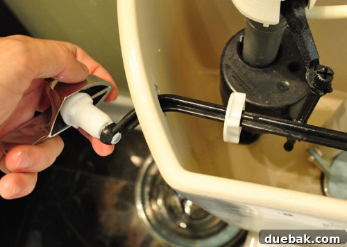 Upgrade Your Toilet with a Dual-Flush Kit 4 Hands removing the old single flush lever from inside a toilet tank during the conversion process.