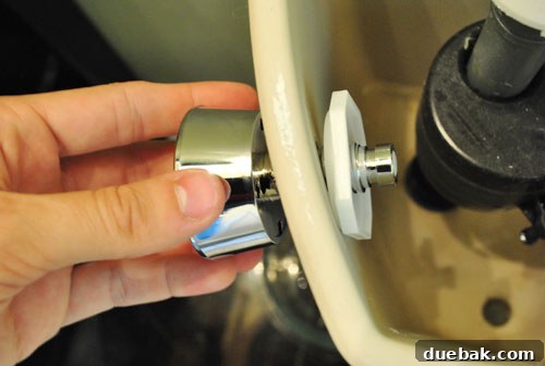 Upgrade Your Toilet with a Dual-Flush Kit 8 A person attaching the new dual flush button assembly to the toilet tank, showing the securing nut.