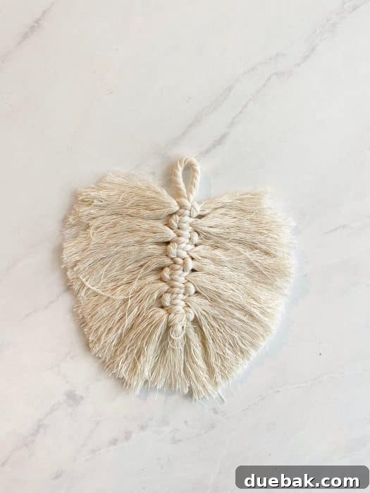 A macrame feather being trimmed with sharp scissors, showing the shaping process.
