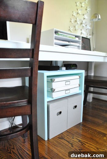 The custom-built storage unit, now painted a soft aqua, neatly holding gray file boxes and white storage bins.