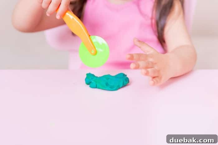 A child's hands pressing a star-shaped cookie cutter into blue playdough on a mat.
