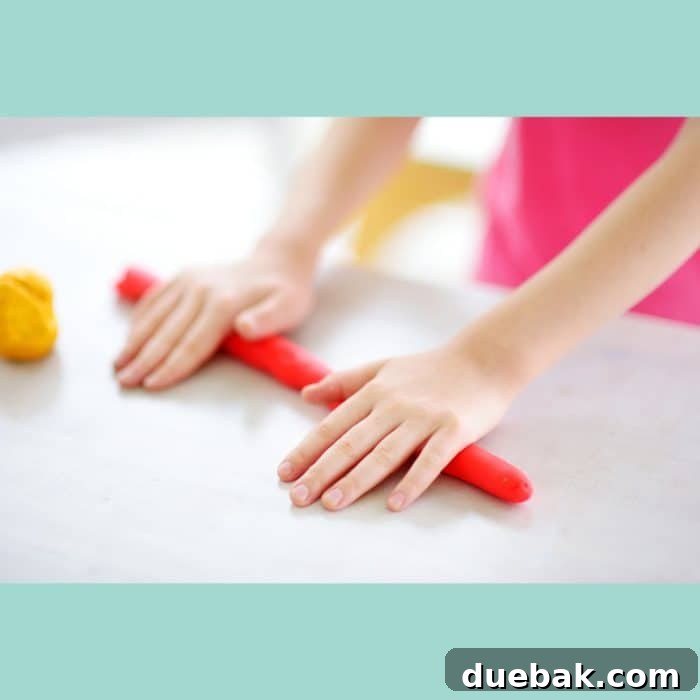 A child's hand using a plastic knife to cut blue playdough on a printable mat.
