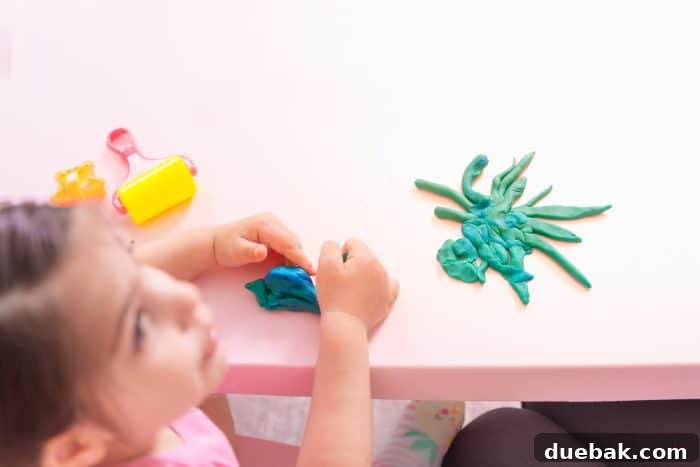 A little girl smiling as she plays with colorful playdough and tools.