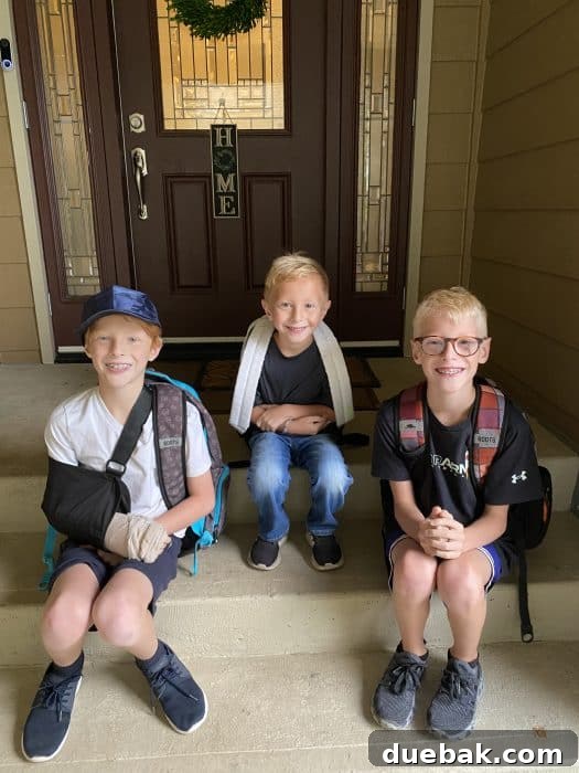 Three boys sitting on a front step with backpacks on, eagerly leaving for their first day of school, holding their first day of school signs.