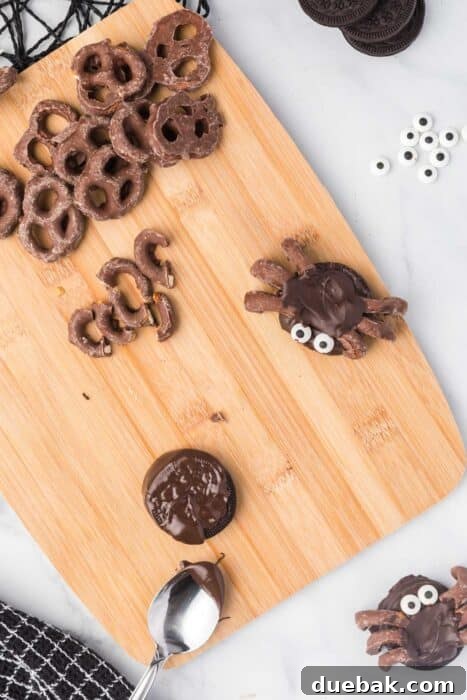 Simple Spooky Spider Treats for Halloween 4 An Oreo cookie partially covered in melted chocolate on a baking sheet, with several chocolate-covered pretzel pieces nearby.