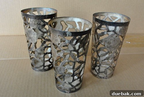 Close-up of three plain, grey metal cups, showcasing their simple design and the cut-out shape that inspired the DIY project. They are resting on a neutral surface.