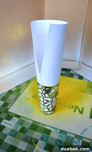 A person's hands demonstrating how to roll up a piece of white paper and insert it into a yellow-painted metal cup to protect the interior during exterior painting.