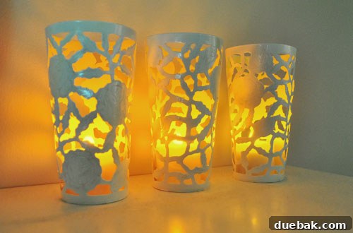 Two newly spray-painted metal cups, one with a flameless candle inside, casting a warm glow from its yellow interior. The cups are displayed as decorative items.