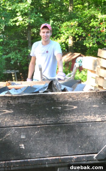 John loading debris into the dumpster from a ladder