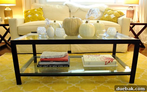 A coffee table decorated for Halloween with faux pumpkins, votive holders, and dried grasses.