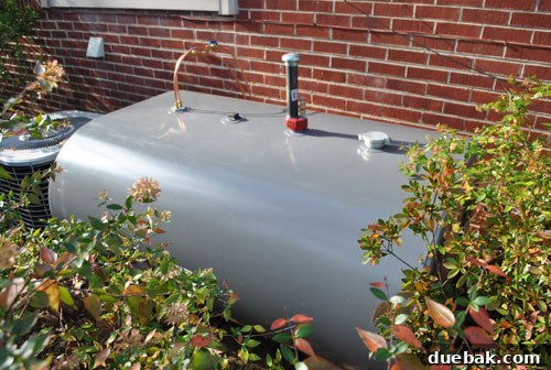 Newly installed above-ground oil tank nestled behind azalea bushes