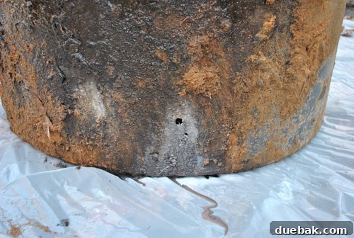 Close-up of a small, dime-sized hole found on the bottom of a rusted oil tank