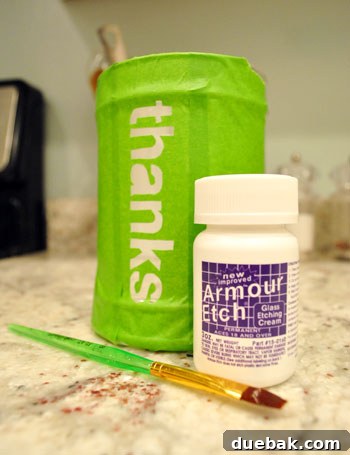 Glass etching cream and paintbrush next to glass jar with DIY tape stencil