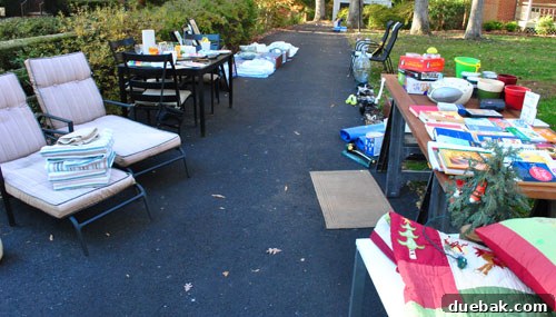Driveway filled with items for sale, bustling with early shoppers.