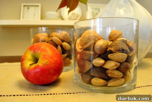 Harvest Home: Autumn Decor Inspiration 5 Clear glass vase filled with mixed nuts and a vibrant red apple, creating a simple fall decoration
