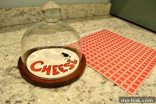 Vintage cheese plate with glass dome and a ceramic insert featuring a black rat design before makeover.