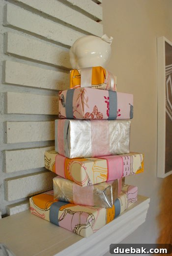 Stacked faux gift boxes in pink, silver, and patterned paper, adorned with ribbons, styled as holiday decor.