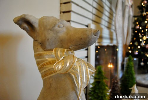 A concrete greyhound statue adorned with a festive gold ribbon around its neck for Christmas.