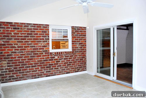 Sunroom featuring an off-centered window and dark brick wall, ripe for transformation