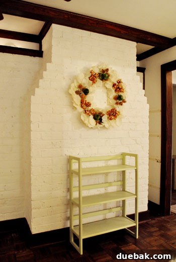 Decking Our New Home for Christmas 3 A classic Pottery Barn holiday wreath hangs on the back of a living room fireplace, offering a touch of festive elegance amidst a room still in transition.