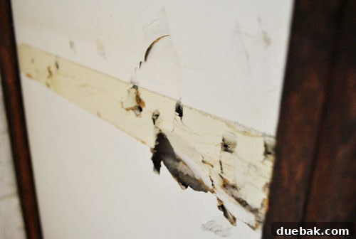 Damaged wall after shelf removal, showing holes and imperfections that need repair