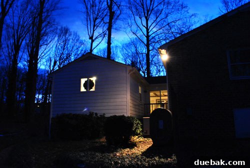 Exterior view of the house at night, showing the bathroom window with minimal visibility into the interior despite lights being on