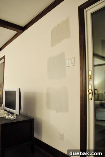 three Benjmain Moore gray paint color swatches on a white wall at night time in artificial light