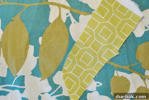 First fabric sample swatch laid on a bed with a green and gold patterned duvet