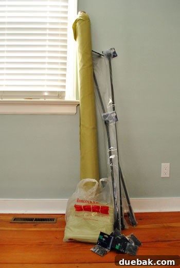 Multiple bolts of avocado-green fabric, curtain rods, and clip rings on a bed
