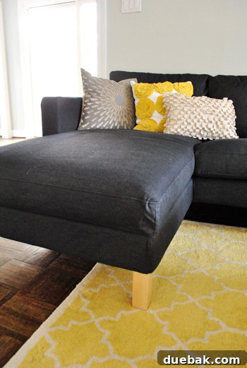Chaise portion of Ikea sectional sofa in dark Sivik gray, invitingly adorned with yellow accent pillows.