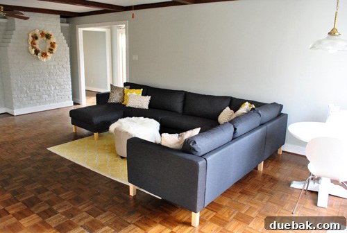 Dark gray Karlstad Ikea sectional sofa freshly assembled in a gray living room, positioned gracefully by the fireplace.