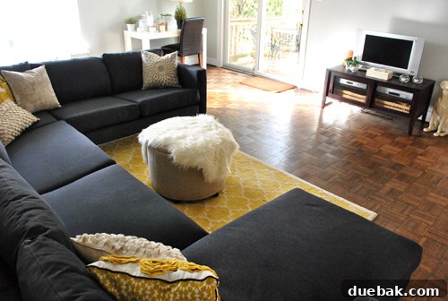 Dark charcoal gray Ikea sectional sofa in a living room, accented by vibrant yellow decorative elements.