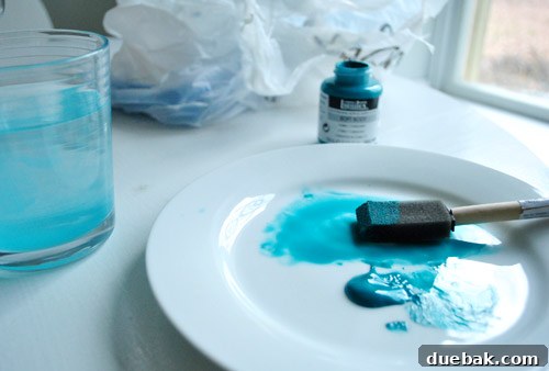A small amount of Cobalt Turquoise acrylic paint diluted with water on a white plate, ready for application with a sponge brush.