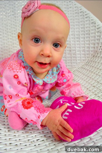 Baby Clara smiling and playing with a red stuffed heart for Valentine's Day.