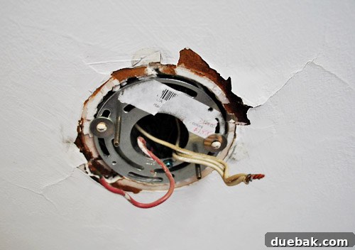 Instant Elegance: Concealing Drywall Cracks with Ceiling Medallions 5 An exposed electrical box on the ceiling with severe cracks and peeling paint clearly visible after the light fixture has been removed.