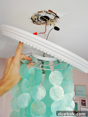 Instant Elegance: Concealing Drywall Cracks with Ceiling Medallions 6 Mid-installation view showing the new light fixture wires threaded through the center of the white ceiling medallion, ready to be reattached to the ceiling.