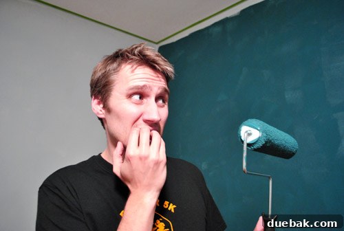 Guest room wall with one coat of dark teal paint, showing patchy coverage.