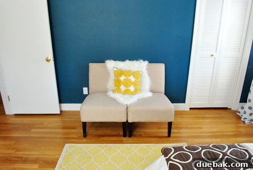 The foot of the bed in the guest room, showing the yellow Pottery Barn rug and two cozy slipper chairs arranged as a small seating area.