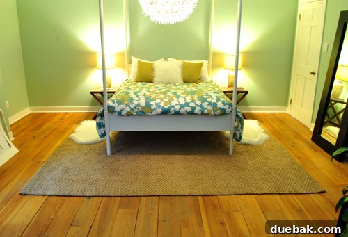 Horizontal placement of a large jute rug in a bedroom, revealing hardwood floor margins around it.