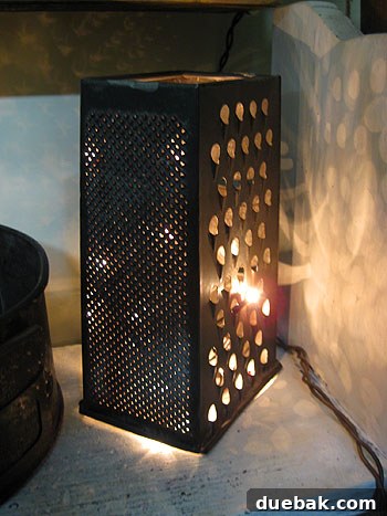 A vintage cheese grater repurposed as a unique light fixture with Christmas lights inside.