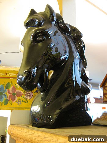 A quirky, open-mouthed ceramic horse head figurine displayed in an antique shop.