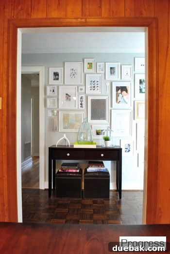 Current view of the hallway through the kitchen doorway, with hung frames and a console table