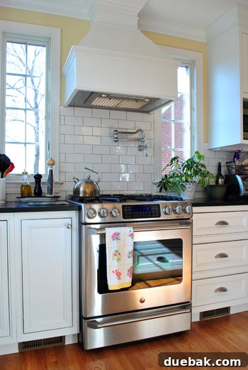 Custom-made range hood over a stove with a pot filler, black honed granite, and white cabinets