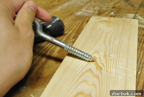 Scraping a coarse screw across a new wood board to create a distressed, abraded effect for a DIY project, mimicking natural wear.