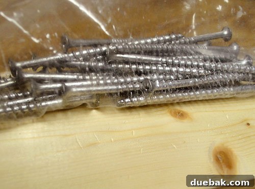Close-up detail of a plastic bag filled with coarse screws being used to create a subtly distressed wood look on a new board for a furniture project.