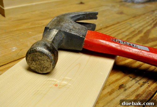 Using a hammer to create intentional dents and impact marks on a new whitewood board, making it appear old, distressed, and reclaimed.
