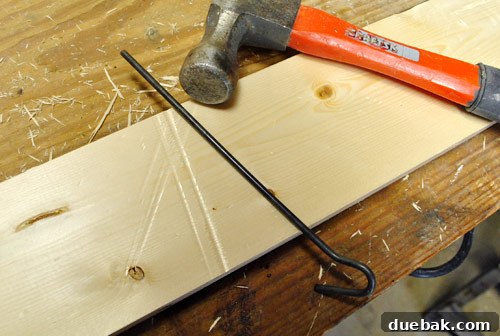 Using a metal rod and hammer to create long, linear dents in a new wood board, simulating years of wear and tear for an aged, beat-up look.