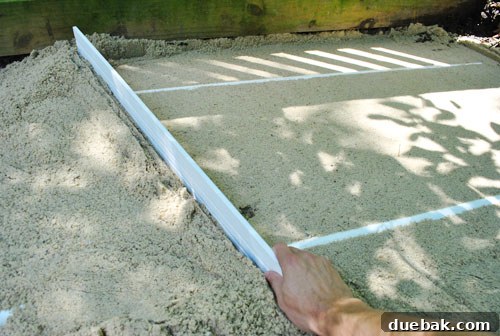 Using a wooden board to screed sand, guided by PVC pipes for a perfectly level surface